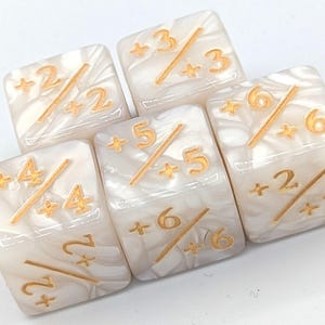 May include: Five square dice with a pearlescent white finish and gold-colored markings. Each die features numbers and a diagonal line, with a plus sign before each number. The dice are for a game.
