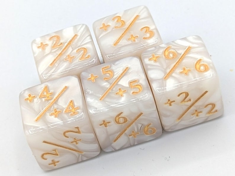 May include: Five square dice with a pearlescent white finish and gold-colored markings. Each die features numbers and a diagonal line, with a plus sign before each number. The dice are for a game.