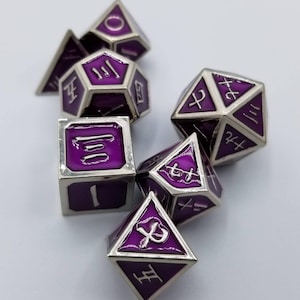 May include: Set of seven purple and silver metal dice with various symbols and numbers on each face. The dice are scattered on a white surface.
