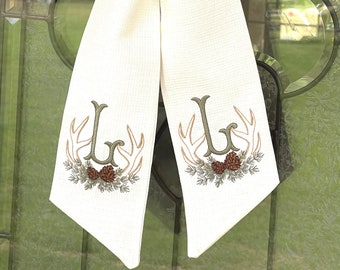 May include: A white fabric door hanger with a monogrammed initial "L" embroidered in green with antlers and pine branches.