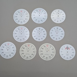 May include: A collection of nine circular watch dials arranged in three rows. Each white dial features black numerical markings for seconds and minutes, with a smaller sub-dial at the top. Some dials display the text Racine Super Select or Yachting Timer.