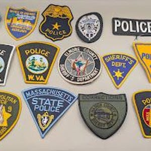Könnte beinhalten: Eine Sammlung von vierzehn bestickten Abzeichen der Strafverfolgungsbehörden in verschiedenen Formen und Farben, darunter Polizei-, Sheriff- und State-Trooper-Embleme mit Texten wie Police, W. Va., Massachusetts State Police und Elmore County Sheriff's Department.