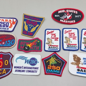 May include: A collection of twelve embroidered bowling patches in various shapes and colors. The patches feature text including YABA 250 Series, National 600 Club, Mid-States Masters, ABC, WIBC, and BCA, along with graphics of bowling pins, balls, and eagles.
