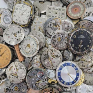 May include: A selection of antique watch components, including watch faces, gears, and internal mechanisms. The parts show signs of age, with visible numbers, hands, and brand names. The color scheme features silver, gold, and black.