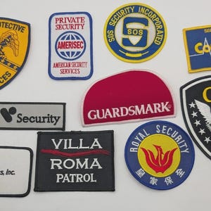 May include: A collection of ten embroidered security patches in various shapes and colours. The patches feature logos and text including Elite Protective Services, Private Security Amerisec, SOS Security Incorporated, Capstat, Guardsmark, and CIS.