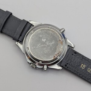 May include: A silver-toned Lucien Piccard watch with a gray leather strap. The watch back is visible, displaying the brand name and model number. The strap is attached to the watch case with silver-toned metal. The watch face is not visible.