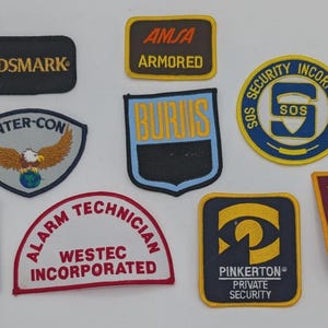 May include: A collection of nine embroidered security patches featuring various shapes and colours. The patches display text including GUARDSMARK, AMSA ARMORED, INTER-CON, BURNS, SOS SECURITY INCORPORATED, CHERRY CREEK SAFETY FACILITIES, ALARM TECHNICIAN WESTEC INCORPORATED, PINKERTON PRIVATE SECURITY, and SECURITY PATROL PASCO COUNTY.
