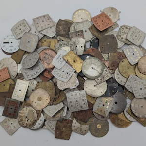 May include: A collection of vintage watch faces in various shapes and sizes. The faces are primarily in shades of white, brown, and gold, with visible numbers and markings. Some faces are square, others round, and some have a rectangular shape.