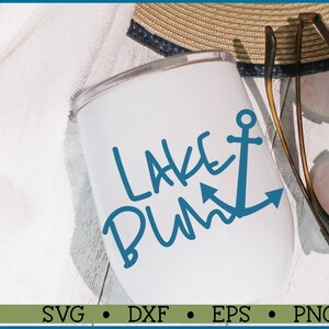 May include: White tumbler with a blue anchor and the text "Lake Bum" in blue cursive writing. The tumbler is sitting on a white wooden surface with a straw hat and sunglasses nearby.