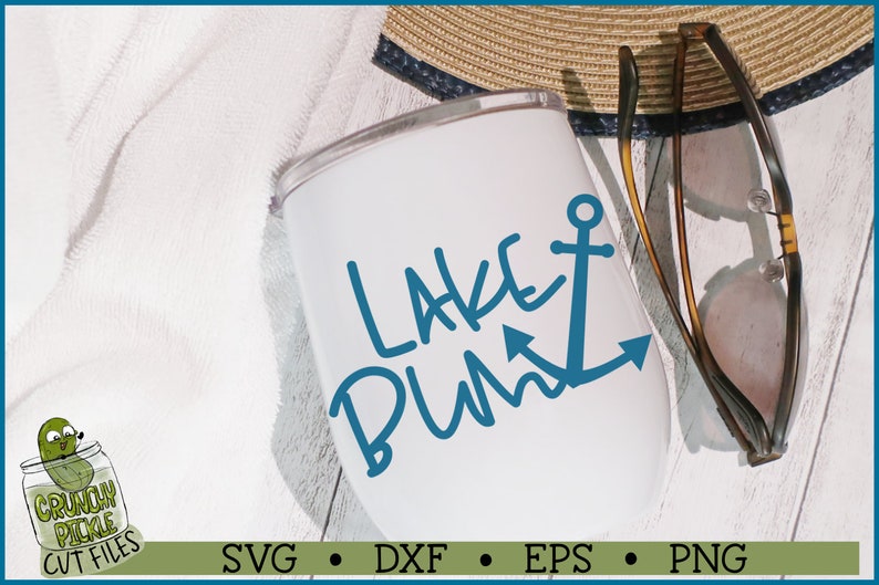 May include: White tumbler with a blue anchor and the text "Lake Bum" in blue cursive writing. The tumbler is sitting on a white wooden surface with a straw hat and sunglasses nearby.