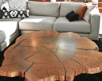 May include: A large, round, wooden coffee table with a natural wood finish and a live edge design. The table has a unique, organic shape and is made from a single piece of wood.