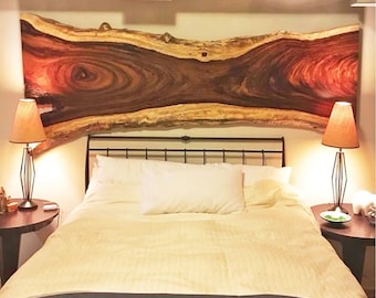 May include: A bedroom with a wooden headboard made from a tree slice. The headboard has a natural wood finish with a reddish-brown hue. The bed has a white duvet and a black and brown patterned throw at the foot of the bed. There are two lamps on nightstands on either side of the bed.