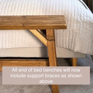 May include: A wooden end-of-bed bench with a natural finish. The bench has a rectangular top and angled support legs. The text on the image reads: "All end of bed benches will now include support braces as shown above."
