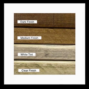 May include: A close-up of four wood samples with different finishes. The top sample is a dark brown, followed by a medium brown, a light white tint, and a clear finish. Each sample has a label indicating the finish type.