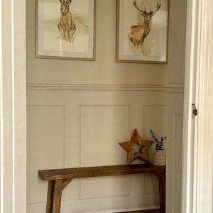 May include: A hallway with framed watercolor art of a hare and a deer above a wooden bench. A wooden star and a small vase with greenery are on the bench. The walls are painted a light beige.