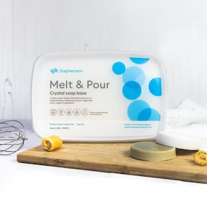 May include: A white rectangular container of Stephenson Melt & Pour Crystal soap base, with blue circular designs. The container sits on a wooden board with soap samples. The text on the container reads "Create a wide range of beautiful products by simply heating, combining colours, fragrances and a range of ingredients."