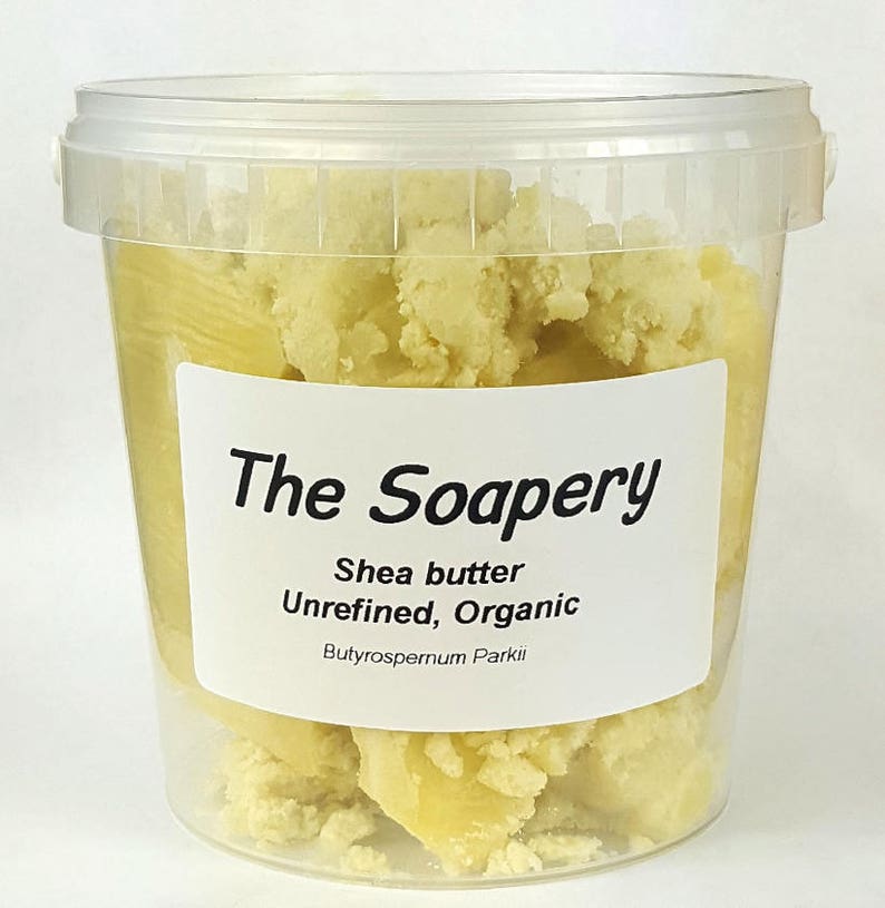 May include: A clear plastic container filled with unrefined, organic shea butter. The container has a white label with the text "The Soapery" and "Shea butter Unrefined, Organic Butyrospermum Parkii".