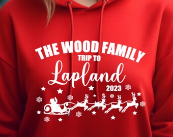 Può includere: Felpa con cappuccio rossa con testo bianco: "THE WOOD FAMILY TRIP TO LAPLAND 2023". Il design include la slitta di Babbo Natale con renne, stelle e fiocchi di neve. Un capo festivo e accogliente.