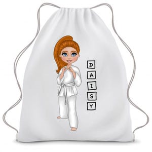 Op de afbeelding: Witte trekkoordtas met een cartoonillustratie van een meisje in een wit karatepak. Het meisje heeft rood haar en blauwe ogen. De naam "DAISY" staat in zwarte vierkanten op de tas.