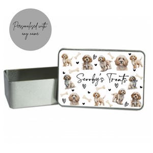 Op de afbeelding: Witte metalen doos met een witte achtergrond en een patroon van bruine en witte honden, botten en harten. De tekst "Scooby's Treats" is in zwart op de doos gedrukt.