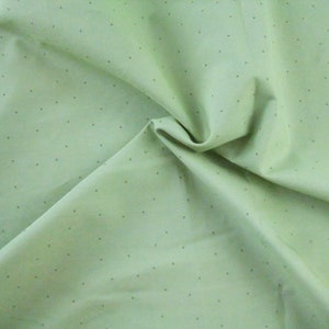 May include: A light green fabric with a subtle white polka dot pattern. The fabric is folded and draped, showcasing its texture and drape.