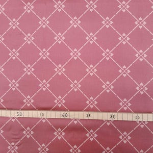 Op de afbeelding: Een close-up van een roze stof met een wit ruitpatroon. De stof heeft een subtiele glans en een zachte textuur. Een liniaal is zichtbaar aan de onderkant van de afbeelding, met markeringen in inches.