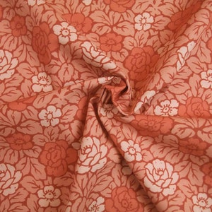 Könnte beinhalten: Nahaufnahme eines Stoffes mit Blumenmuster. Der Stoff ist in einem Pfirsich-Orange-Ton mit weißen Blüten und Blättern.
