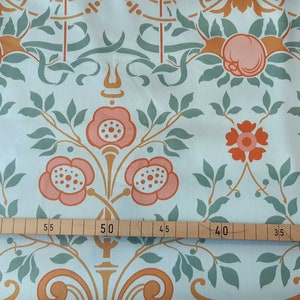 Könnte beinhalten: Ein hellblauer Stoff mit einem sich wiederholenden Muster aus stilisierten Blumen und Blättern in Orange-, Rosa- und Grüntönen. Der Stoff wird mit einem Lineal in Zentimetern gemessen.