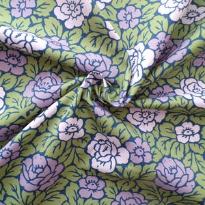 Könnte beinhalten: Ein Stoff mit einem Blumenmuster. Der Stoff ist grün mit rosa und weißen Blumen. Die Blumen sind stilisiert und haben einen Vintage-Look.