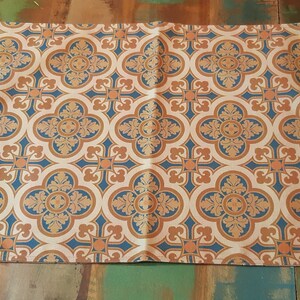 May include: Beige rectangular placemat featuring a repeating pattern of blue and orange floral quatrefoils. The design is symmetrical, with each floral element enclosed within a circular shape. The placemat is made of a woven fabric.