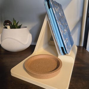 May include: A cream-colored tablet stand with a cork coaster and a blue tablet case featuring a floral design. A small succulent plant in a white pot is also visible.