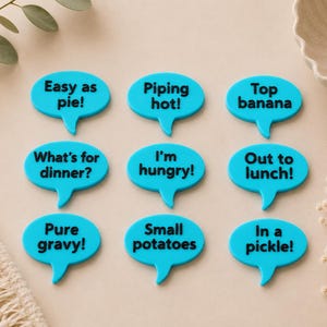 May include: Nine bright blue speech bubble magnets featuring black text: Easy as pie!, Piping hot!, Top banana, What's for dinner?, I'm hungry!, Out to lunch!, Pure gravy!, Small potatoes, and In a pickle! Each bubble has a small tail.