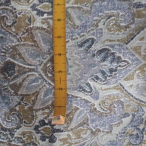 Könnte beinhalten: Nahaufnahme eines Stoffes mit Paisley-Muster in Blau-, Grau- und Brauntönen. Ein gelbes Lineal ist vertikal platziert und zeigt die Maße in Zentimetern an. Der Stoff hat ein strukturiertes Aussehen.