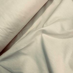 以下が含まれることがあります： 柔らかい折り目と丸まった端を持つ、明るいベージュ色の生地のクローズアップ。素材は滑らかで、リネンまたは同様のテキスタイルである可能性があります。照明は、生地の質感とドレープを強調する影を作り出しています。