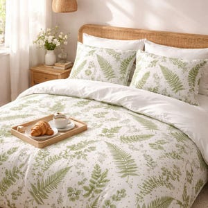 May include: White bedding set with a green fern leaf pattern. The set includes a duvet cover and two pillowcases. A wooden tray with a croissant and coffee cup sits on the bed. The bed has a woven headboard.