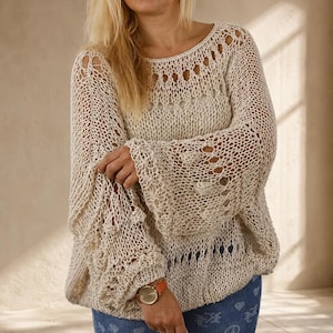 Hand knit off white cotton boho sweater with oversized fit, open knit texture and dramatic bell sleeves, shown in soft natural window light.