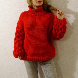 May include: A red knitted sweater with a turtleneck and large, open-weave sleeves.