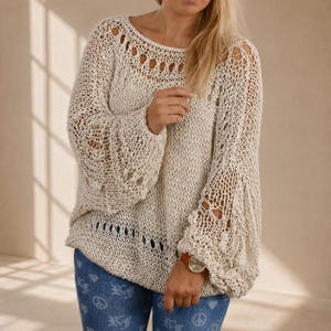 Hand knit off white cotton boho sweater with open knit texture, oversized fit and wide bell sleeves, shown in soft natural window light.
