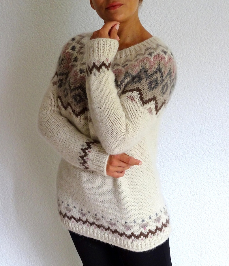 Wrap yourself in softness with this stunning hand-knit Icelandic-style sweater in creamy white tones with subtle Fair Isle patterns in earthy brown, soft grey, and blush pink. This cozy pullover is the perfect blend of rustic charm and modern elegance – a beautiful staple for winter.