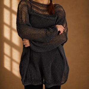 Puede incluir: Un suéter de punto gris oscuro con tejido abierto y mangas largas. El suéter tiene un ajuste holgado y de gran tamaño y un cuello barco. Las mangas son anchas y el dobladillo es ligeramente más largo en la espalda. El suéter está hecho de un hilo suave y texturizado.