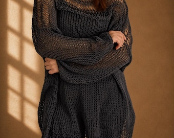 May include: A dark gray, open-weave knit sweater with long sleeves. The sweater has a loose, oversized fit and a boat neckline. The sleeves are wide and the hemline is slightly longer in the back. The sweater is made of a soft, textured yarn.