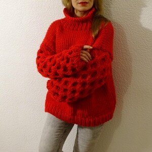 May include: A red knitted sweater with a high neck and large, open-weave sleeves.