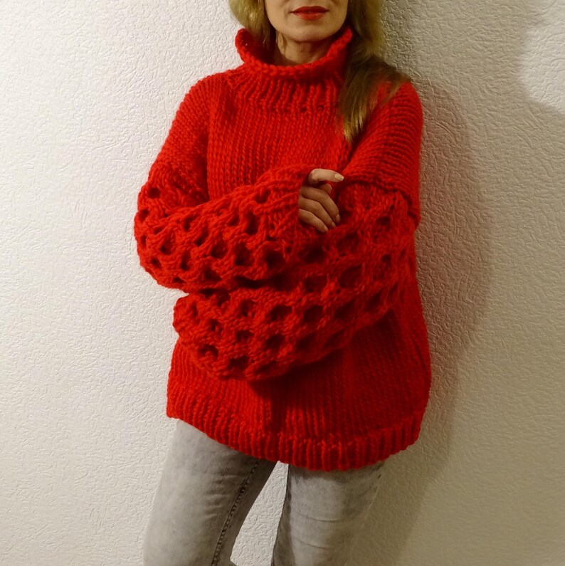 May include: A red knitted sweater with a high neck and large, open-weave sleeves.
