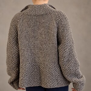 Straight back view of a wool cardigan showing the smooth central knit panel, textured sleeves and lower edge.