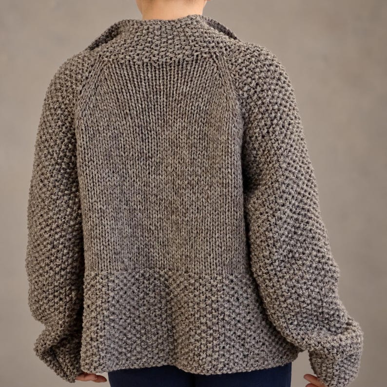 Straight back view of a wool cardigan showing the smooth central knit panel, textured sleeves and lower edge.