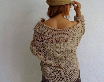 May include: A beige, open-weave crochet sweater with long sleeves. The sweater has a wide, off-the-shoulder neckline and is paired with a straw hat. The back of the sweater has a unique, open design.