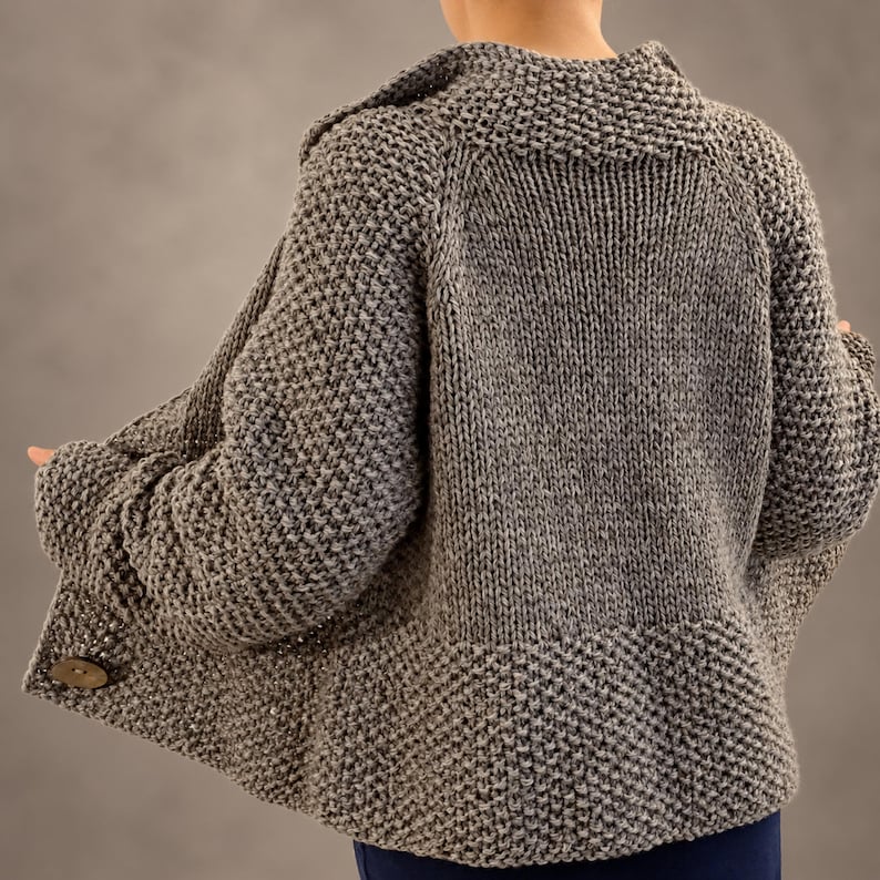 Three quarter back view of a Ash brown hand knit wool cardigan showing its relaxed shape and contrasting knit textures.