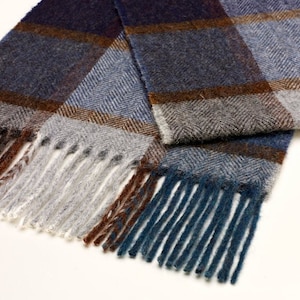 May include: A blue and brown plaid scarf with fringe tassels. The scarf is folded in half and the tassels are visible on both ends.