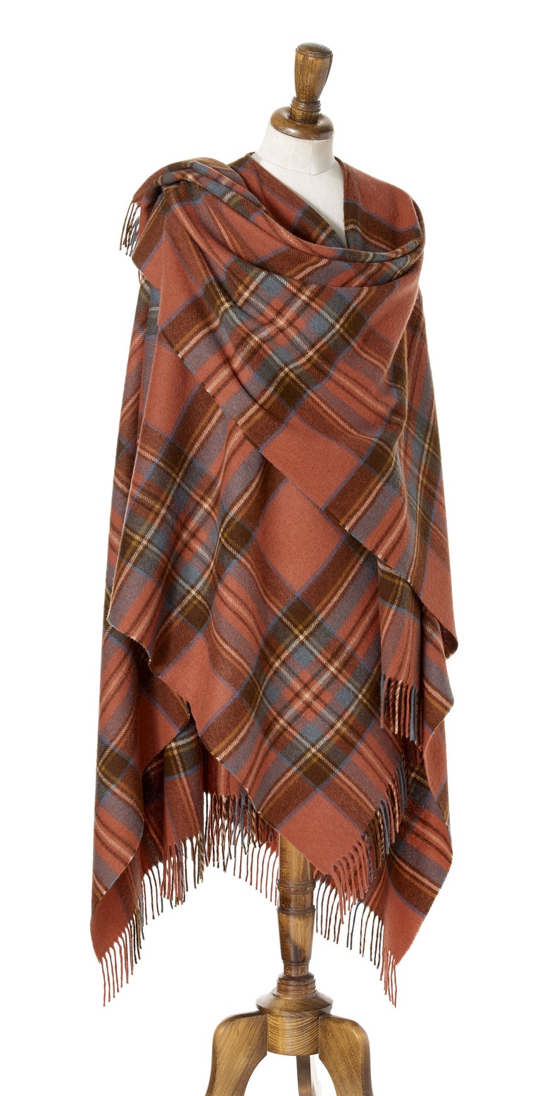 May include: A rust-colored plaid shawl with fringe on a wooden mannequin. The shawl is folded in a triangular shape and draped over the mannequin's shoulders.