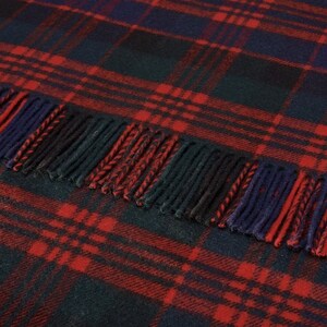 May include: A red, black, and blue plaid throw blanket with fringe. The blanket is made of soft, warm wool and is perfect for snuggling up on the couch.
